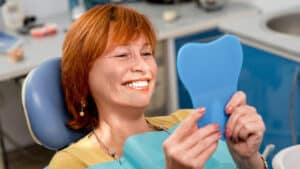 lady smiling while looking into a mirror after getting dental implants